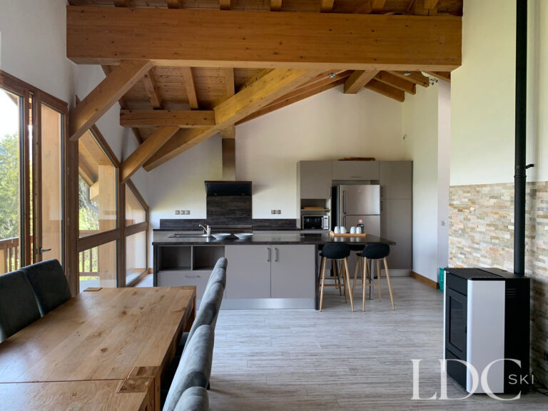 Open-plan dining area and kitchen beneath exposed timber beams at Chalet Edelweiss