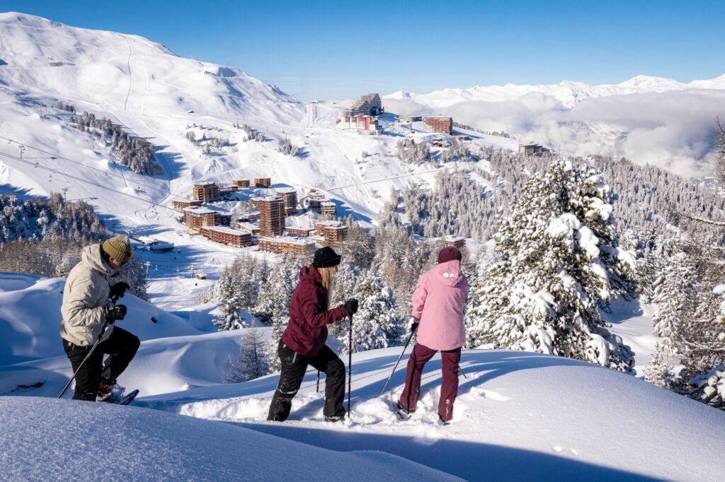 Snowshoers overlooking the snowy resort and mountains of La Plagne – © JNJ Photo / La Plagne