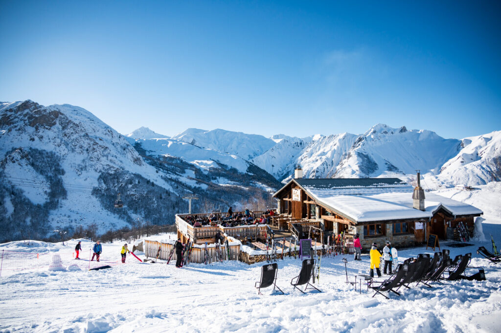 Skiers outside a mountain restaurant overlooking the snowy peaks above St Martin de Belleville