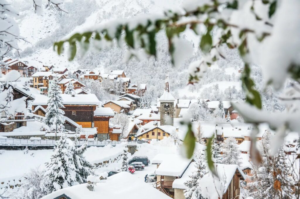 Snow-covered traditional village framed by trees in St Martin de Belleville