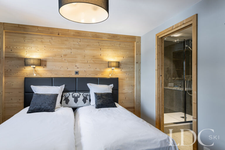 Twin bedroom at Prestige No.5 with timber feature wall and adjoining en-suite shower room