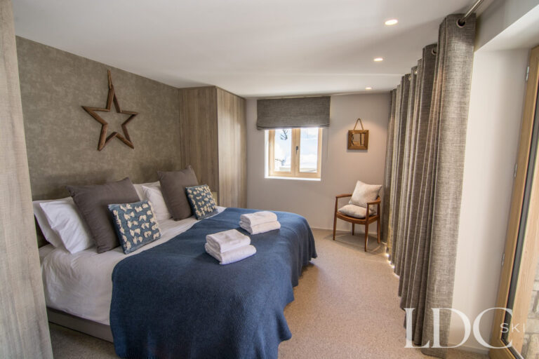 Spacious double bedroom with blue furnishings and alpine-style décor at Chalet Astilla in St Martin de Belleville