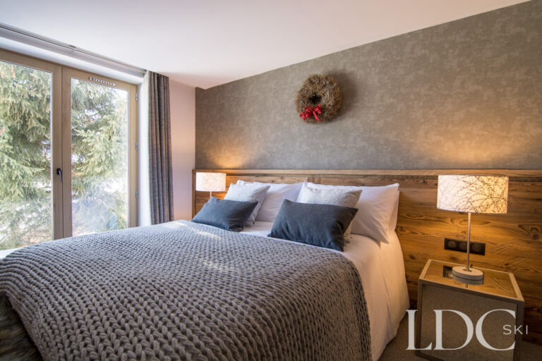 Comfortable double bedroom with grey furnishings and wooden headboard at Chalet Astilla in St Martin de Belleville