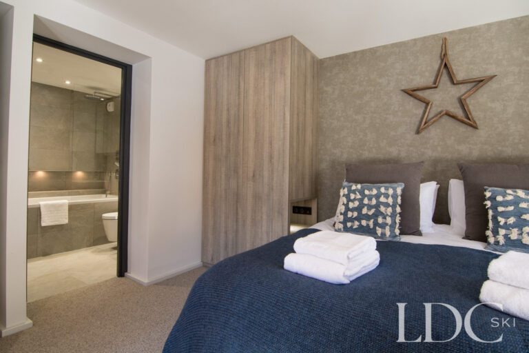 Double bedroom with blue furnishings and adjoining bathroom at Chalet Astilla in St Martin de Belleville