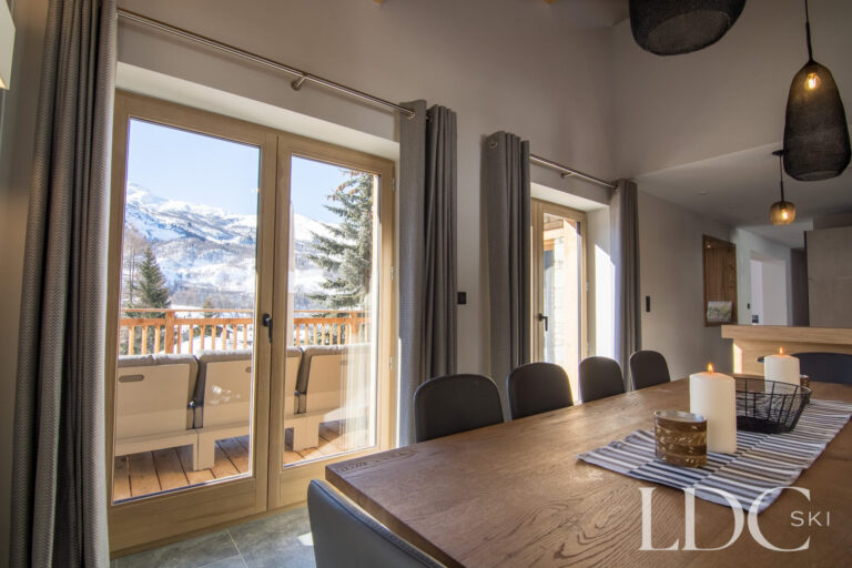 Dining table beside large windows overlooking the snowy mountains at Chalet Astilla in St Martin de Belleville