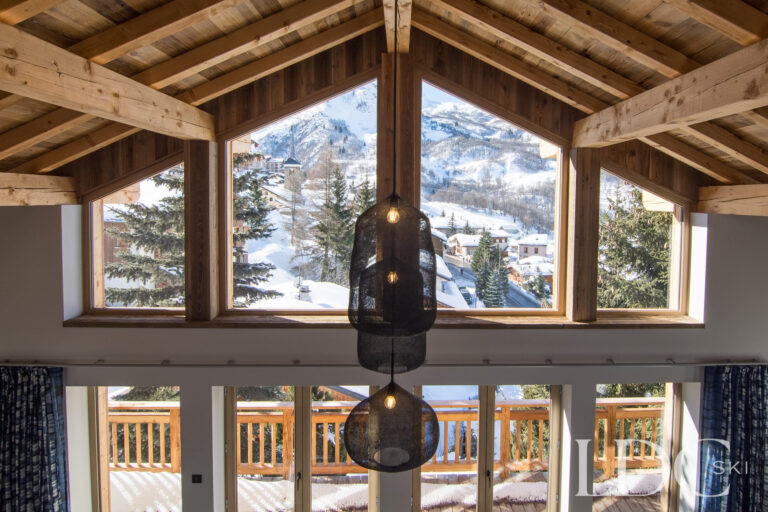 Chalet Astilla lounge with floor-to-ceiling windows overlooking the snowy mountains in St Martin de Belleville