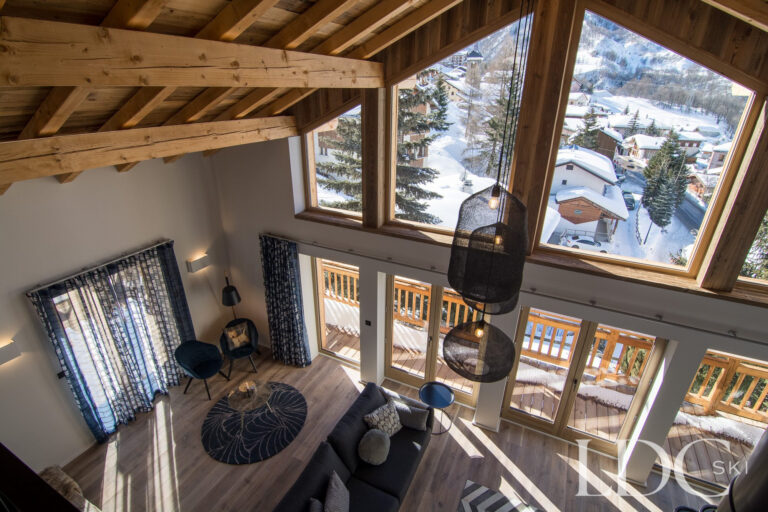 Double-height lounge at Chalet Astilla with large windows and snowy mountain views in St Martin de Belleville