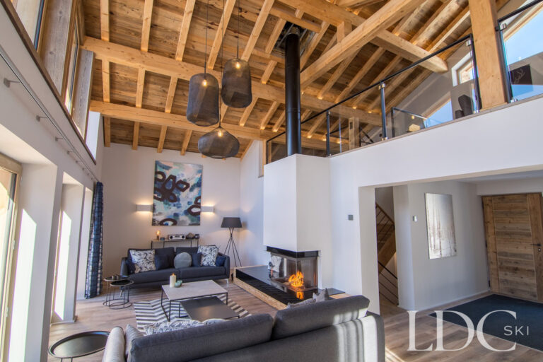Double-height lounge with floor-to-ceiling windows overlooking the snowy mountains at Chalet Astilla in St Martin de Belleville