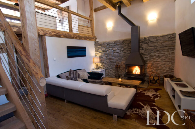 Double-height lounge at Chalet Ann with exposed stone walls, timber beams and log-burning fireplace