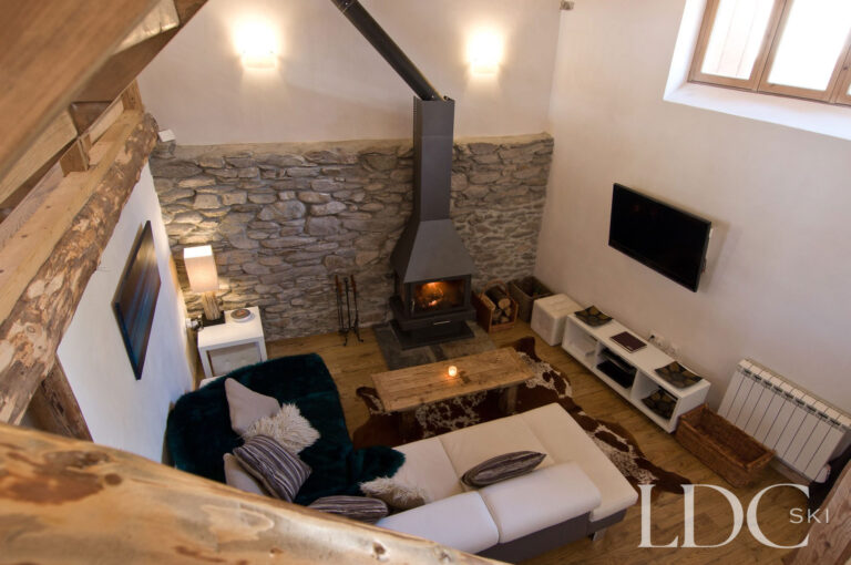 View from the mezzanine into the lounge at Chalet Ann with stone fireplace and exposed beams