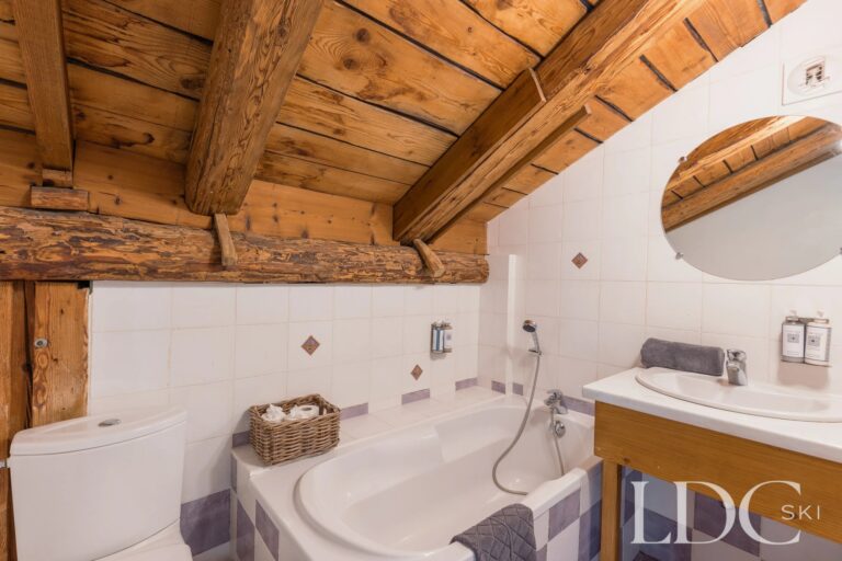 Bathroom with corner bath and exposed timber beams at Chalet Aux Joux