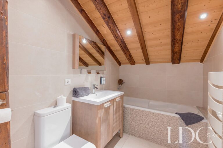 Bathroom with bath and sloping timber ceiling at Chalet Aux Joux