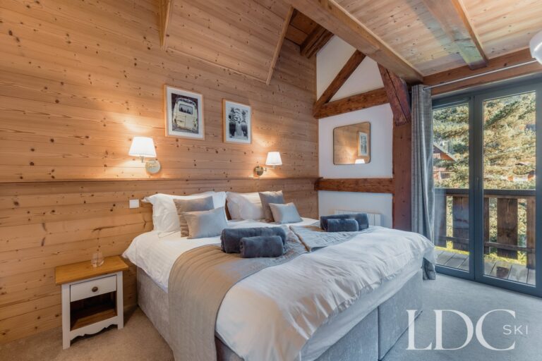 Double bedroom with timber walls and doors opening onto the balcony at Chalet Aux Joux