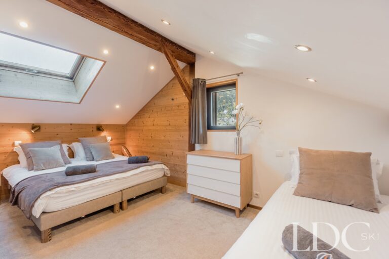 Triple bedroom with double and single beds beneath a sloping ceiling at Chalet Aux Joux