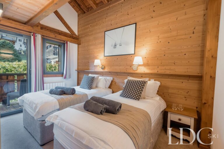 Twin bedroom with timber walls and balcony doors at Chalet Aux Joux