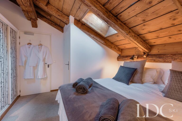Cosy double bedroom beneath exposed timber beams at Chalet Aux Joux