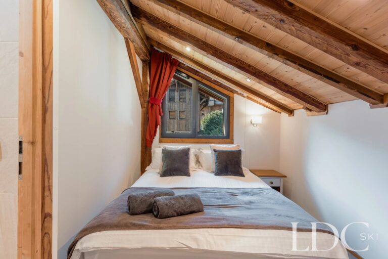 Cosy double bedroom beneath a sloping timber ceiling at Chalet Aux Joux