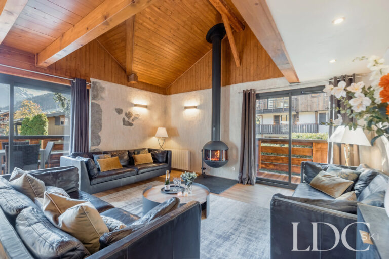 Bright chalet lounge with sofas, fireplace and large windows at Chalet Aux Joux