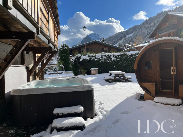 Snow-covered garden with outdoor sauna and mountain views at Chalet Aux Joux