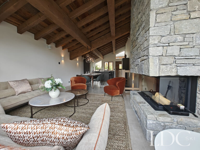 Spacious Alpine living room with large stone fireplace and vaulted timber ceiling at Chalet Chardon in St Martin de Belleville
