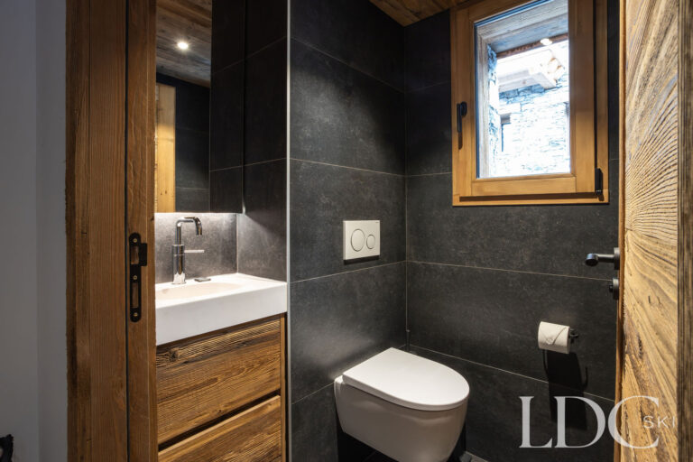 Contemporary guest WC with dark stone tiling and wooden vanity at Chalet de Beauvoir