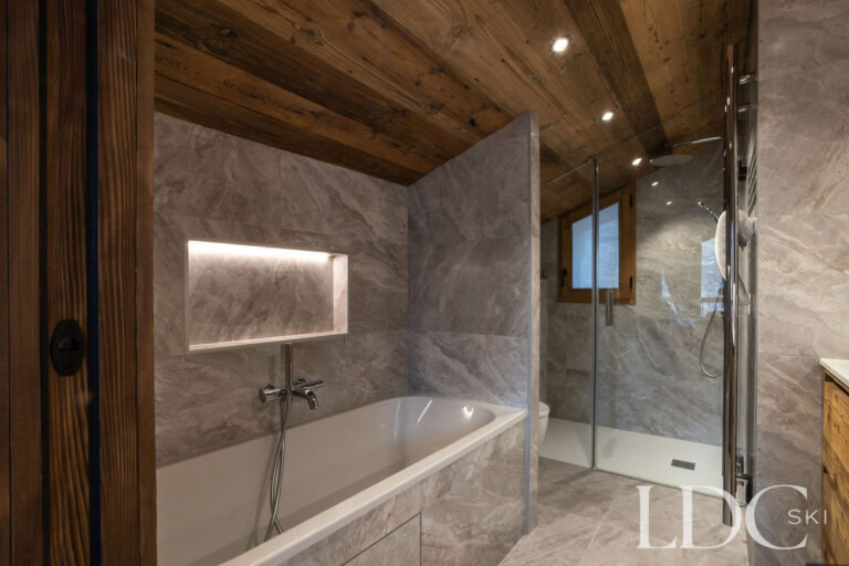 Stone-tiled bathroom with bath and separate walk-in shower at Chalet de Beauvoir