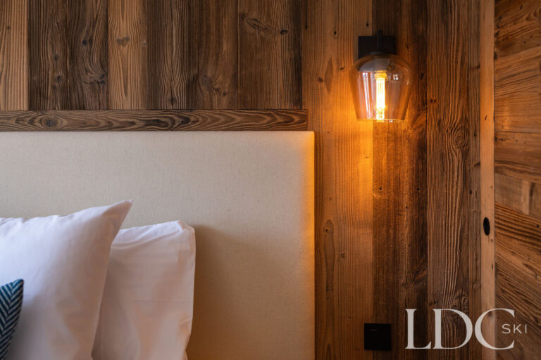 Bedroom detail at Chalet de Beauvoir showing upholstered headboard, reclaimed wood and warm bedside lighting