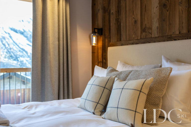 Double bedroom detail at Chalet de Beauvoir with alpine-style cushions, wood panelling and mountain views
