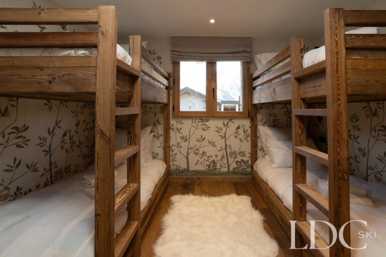 Four-person bunk room at Chalet de Beauvoir with two sets of wooden bunk beds and botanical wallpaper