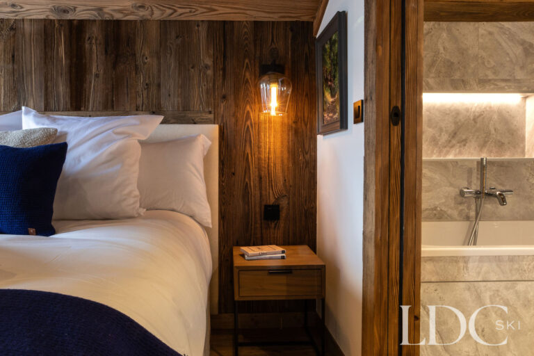 Double bedroom with timber interior and adjoining en-suite bathroom at Chalet de Beauvoir
