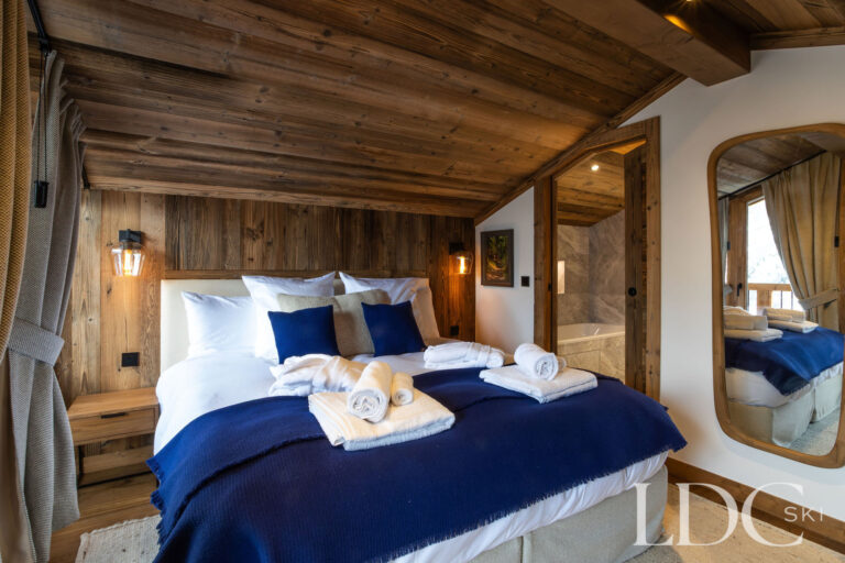 Double bedroom with timber walls, blue soft furnishings and en-suite bathroom at Chalet de Beauvoir