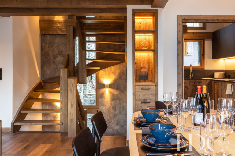 Dining area at Chalet de Beauvoir with laid table, wooden staircase and adjoining kitchen