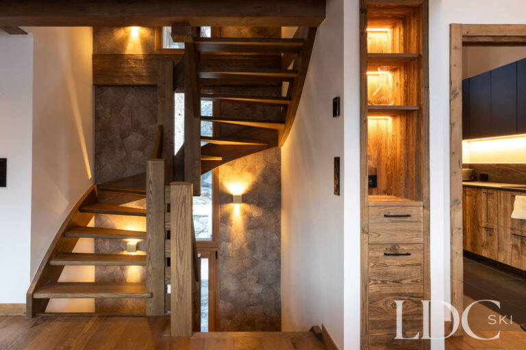 Warmly lit wooden staircase and dining area at Chalet de Beauvoir with contemporary alpine interiors