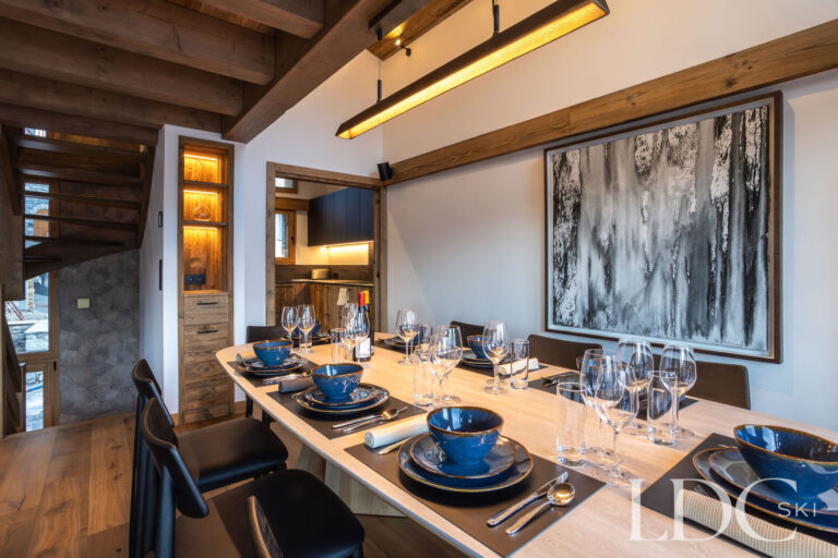 Dining table at Chalet de Beauvoir laid for guests with contemporary alpine interiors and adjoining kitchen