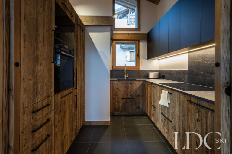 Contemporary kitchen at Chalet de Beauvoir with wood cabinetry, dark worktops and integrated appliances