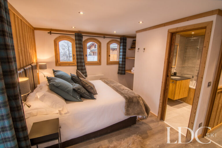 Double bedroom at Chalet Astragle with timber panelling and adjoining en-suite shower room