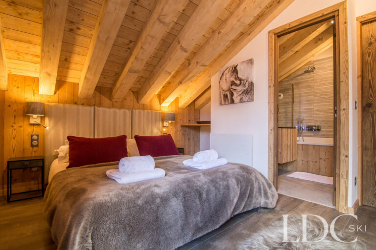 Double bedroom at Chalet Astragle beneath a vaulted timber ceiling with en-suite shower room