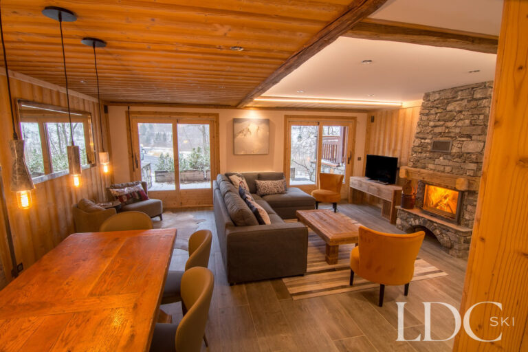 Open-plan living and dining area at Chalet Astragle with log fire, timber ceiling and large windows