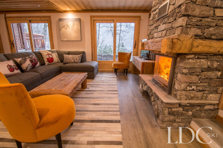 Cosy lounge at Chalet Astragle with sofas, armchair and log fire in a stone fireplace
