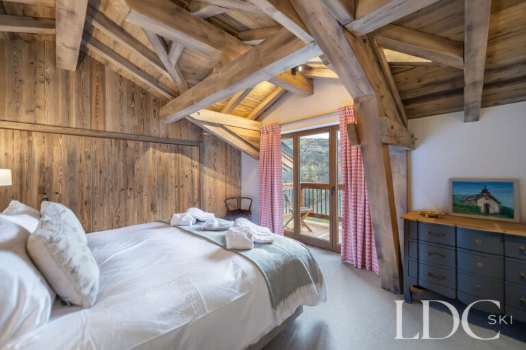 Double bedroom at Chalet La Fermette with exposed timber beams and doors opening onto a balcony