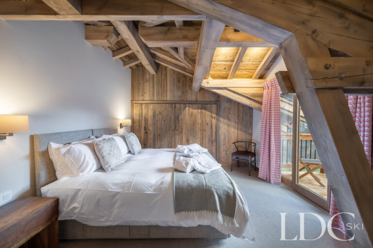 Double bedroom at Chalet La Fermette with exposed timber beams and balcony access
