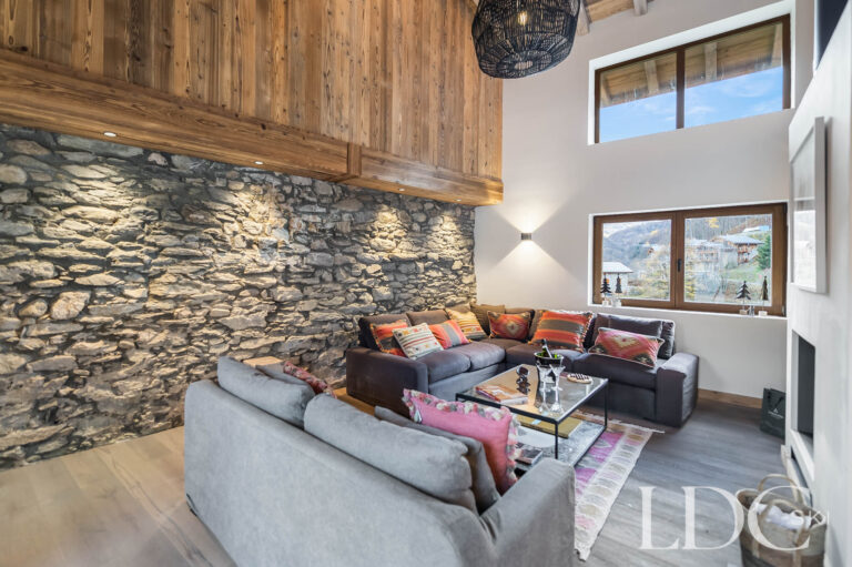 Lounge at Chalet La Fermette with sofas, exposed stone wall and double-height ceiling