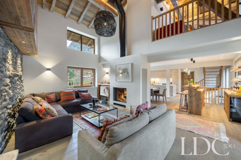 Open-plan lounge at Chalet La Fermette with exposed stone, timber beams and mezzanine above