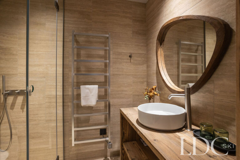Alpine-style bathroom at Chalet Lenafaju with round mirror, basin and heated towel rail