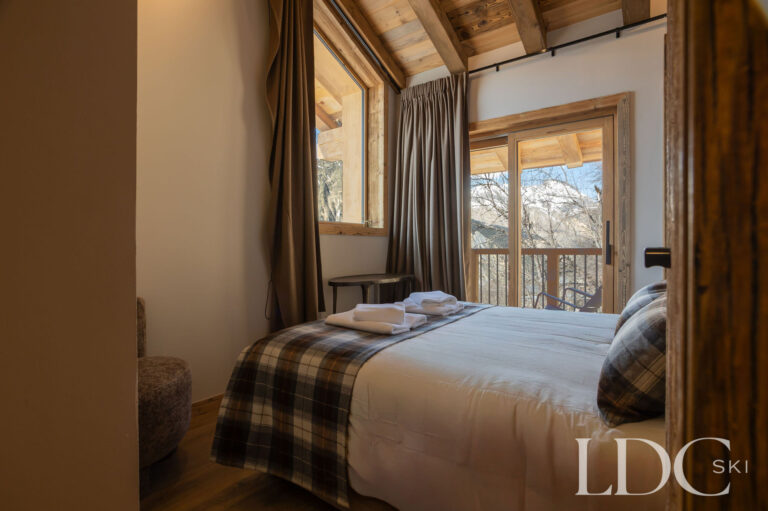 Double bedroom at Chalet Lenafaju with timber ceiling and doors opening towards the balcony