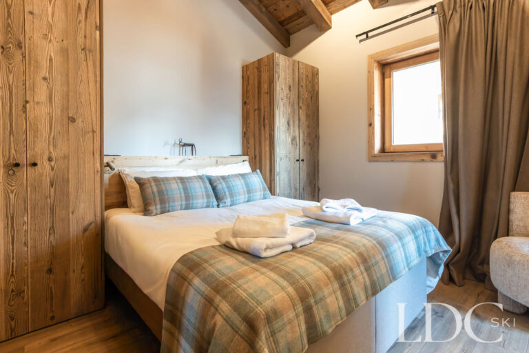 Double bedroom at Chalet Lenafaju with wood-panelled walls and checked alpine-style bedding