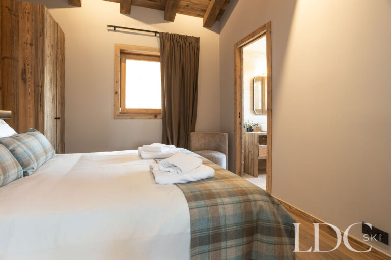Double bedroom at Chalet Lenafaju with wood panelling and adjoining en-suite bathroom