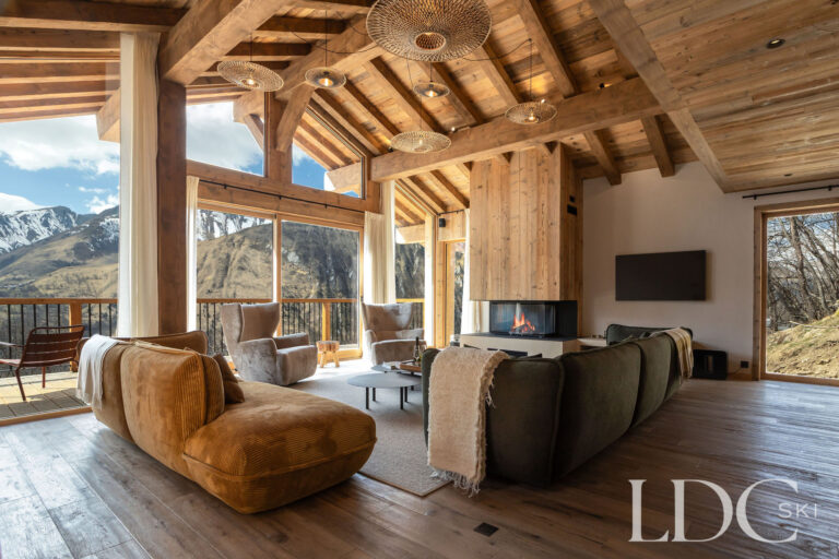 Lounge at Chalet Lenafaju with fireplace, timber ceiling and panoramic mountain views