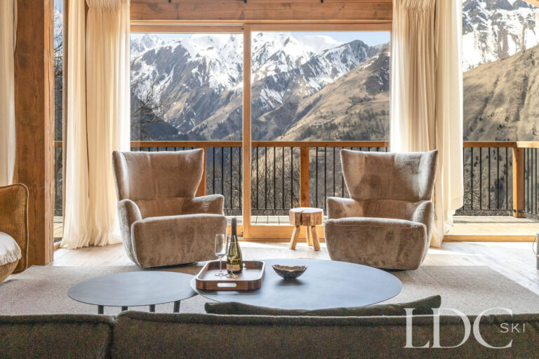 Lounge seating at Chalet Lenafaju beside floor-to-ceiling windows with panoramic mountain views in St Martin de Belleville
