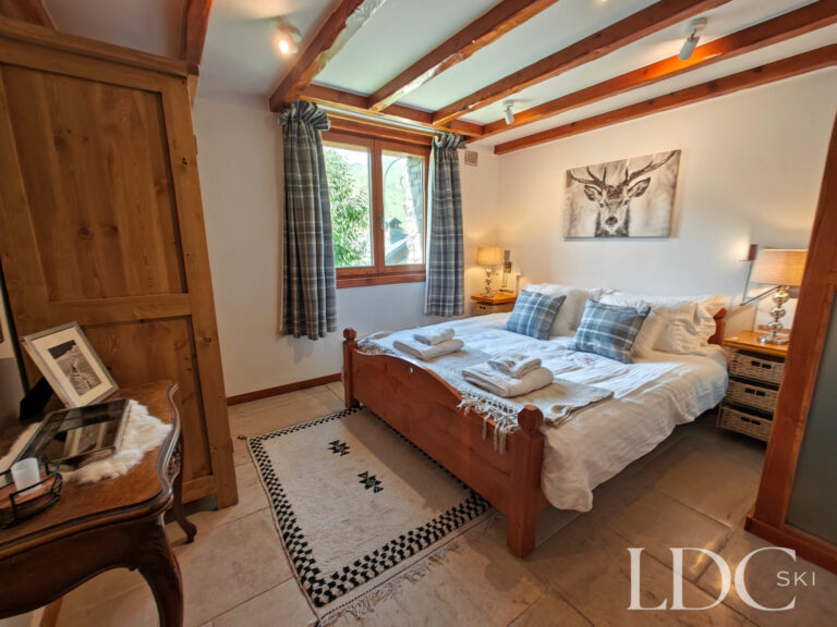 Double bedroom at Chalet Malina with exposed timber beams, wooden bed and large window